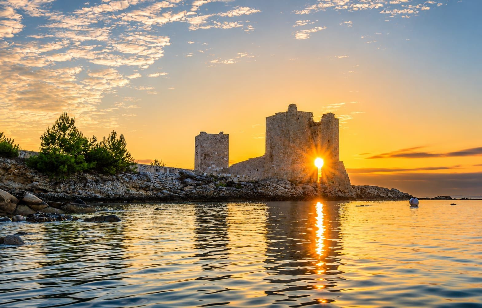 The Kaštelina fortress on the shore of Vir at sunrise, the sun low between its walls