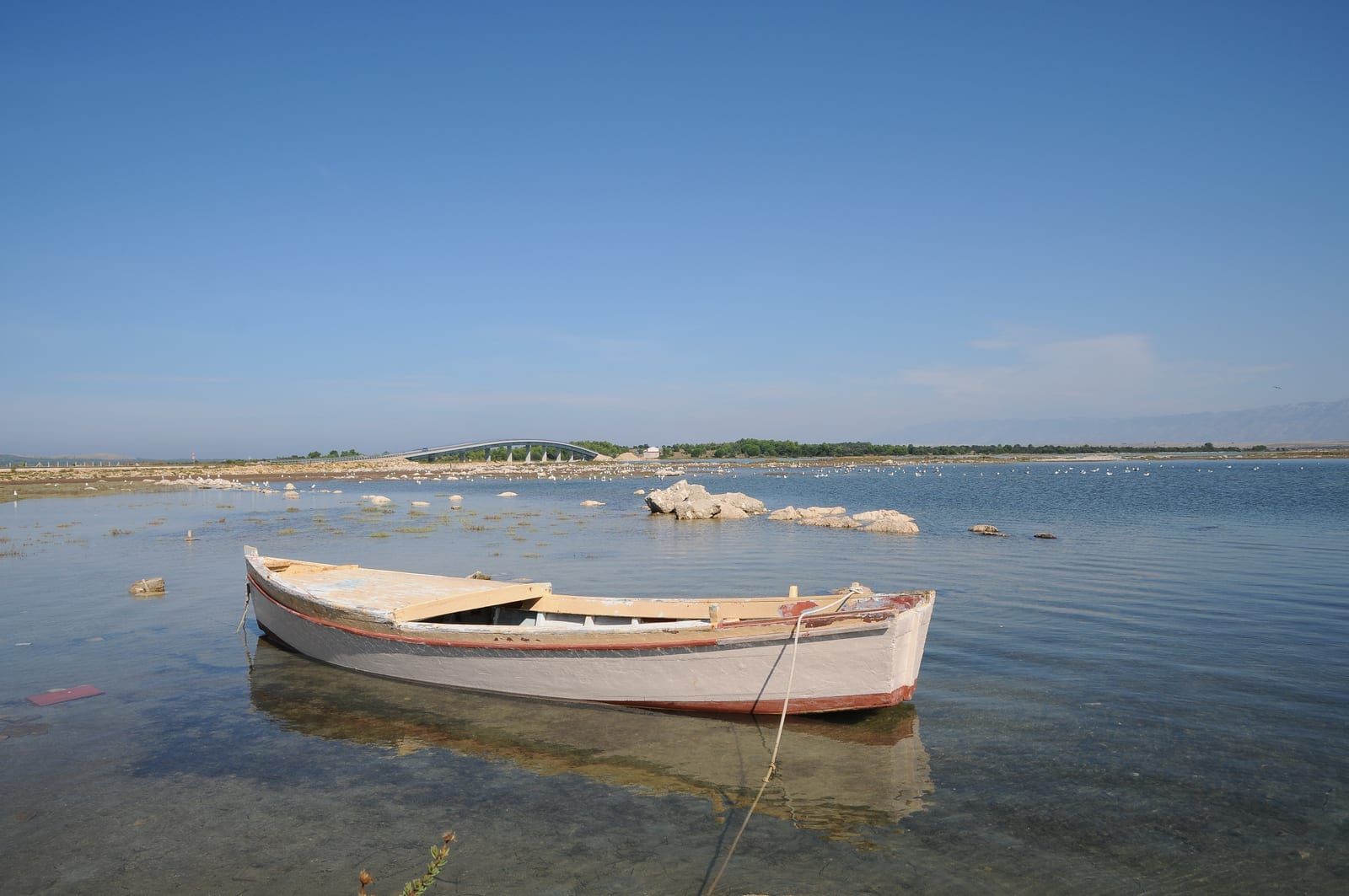 A wooden fishing boat in shallow clear water at Privlaka, with the Velebit range behind