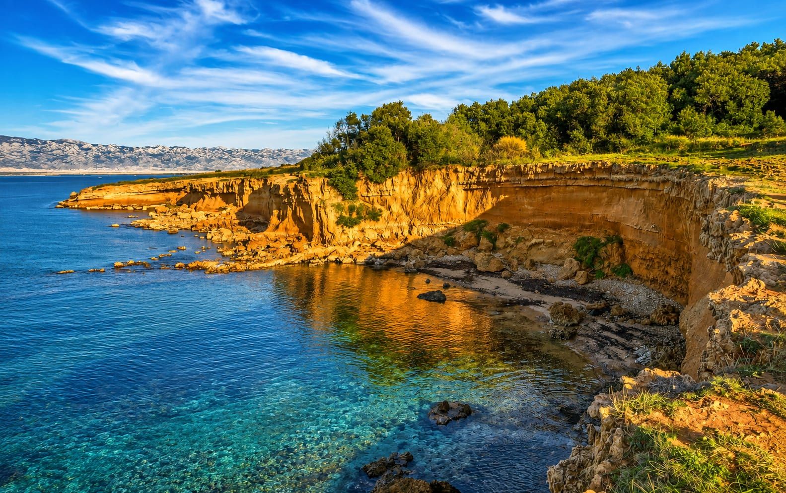 The red rock coast of Vir with turquoise water and the Velebit range behind