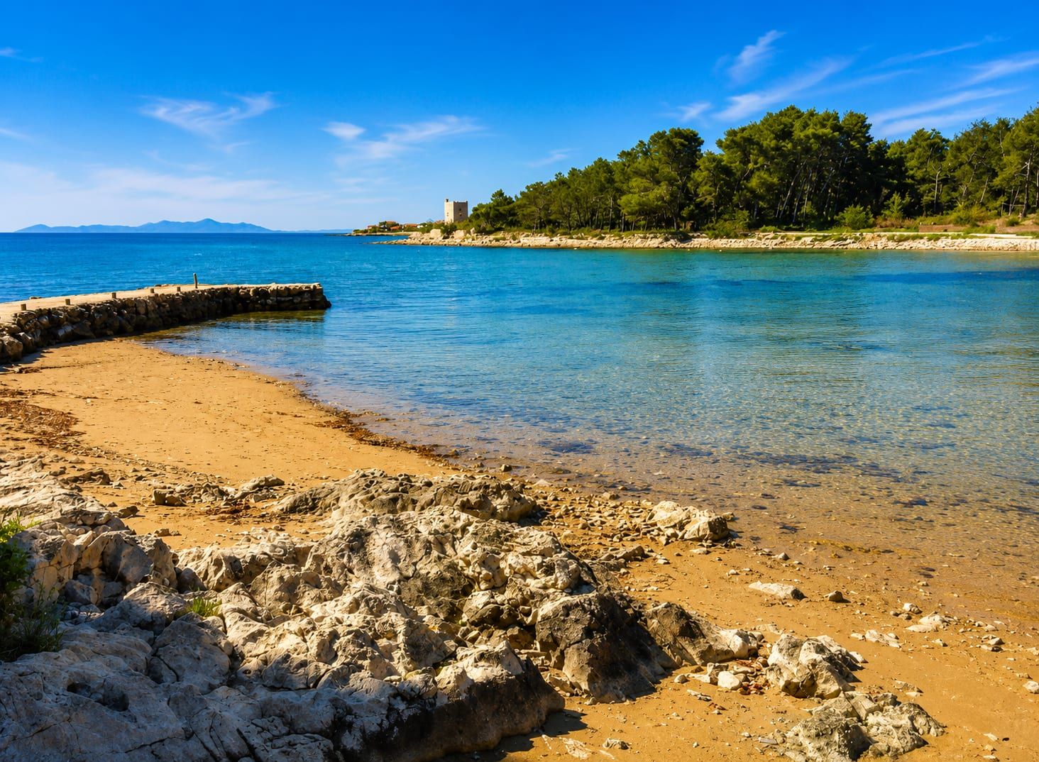 The sandy beach at Sapavac with a stone pier, the Kaštelina tower in the distance